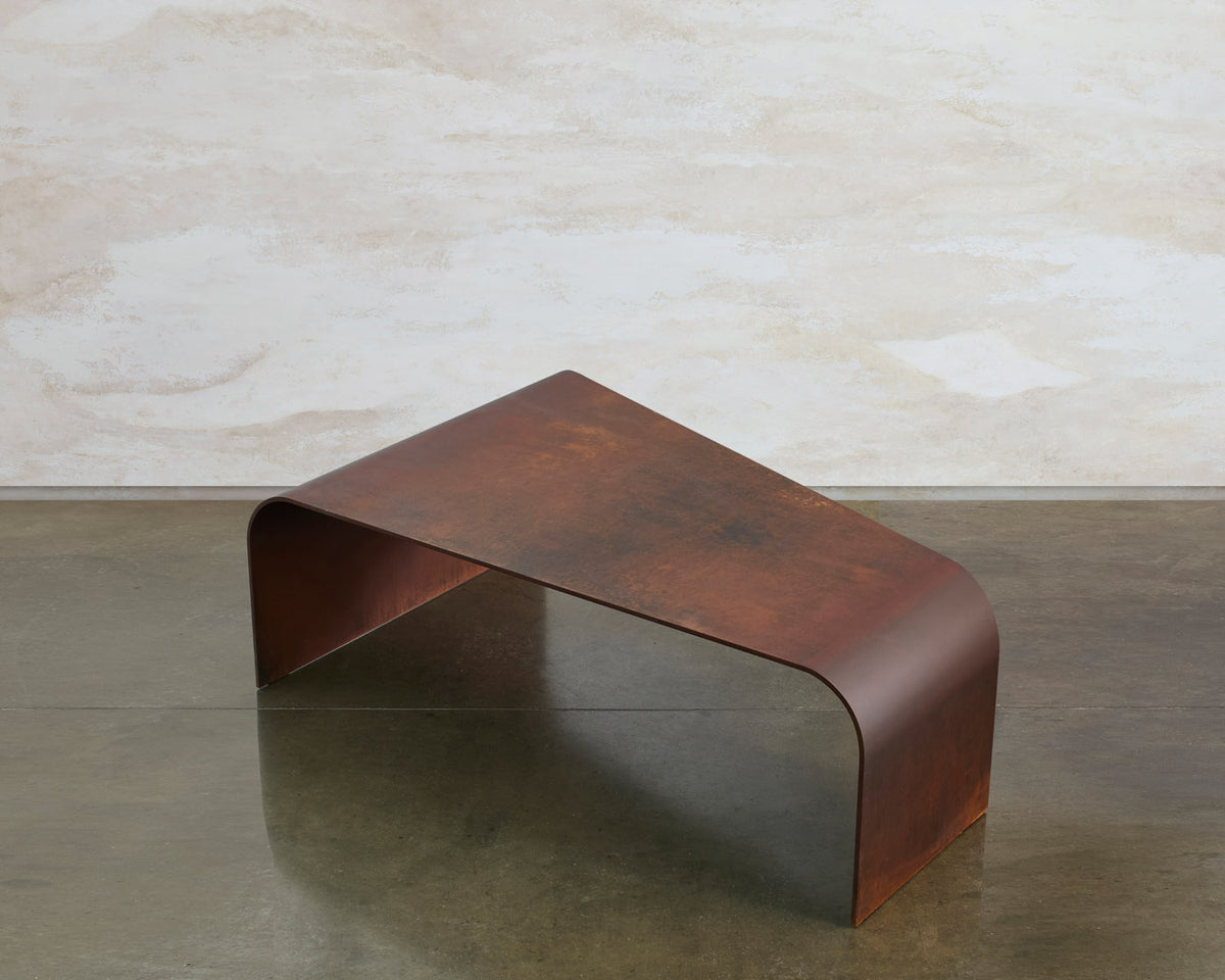 Perception coffee table by Tala Fustok Studio, a tapered corten steel form with a curved end on a polished concrete floor