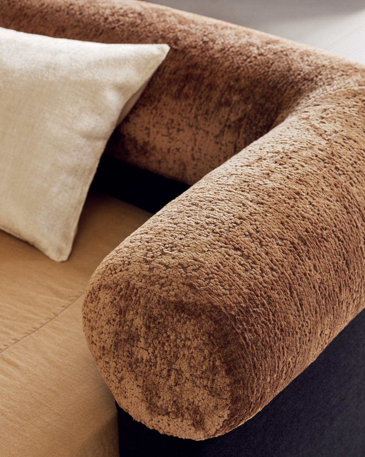 Close-up of the Nest bed’s textured rust velvet bolster rail, charcoal base, and cream linen cushion
