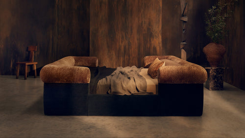 Sculptural Nest bed by Tala Fustok Studio, with a rust velvet bolster rail, charcoal base, and linen throw against a dark timber wall