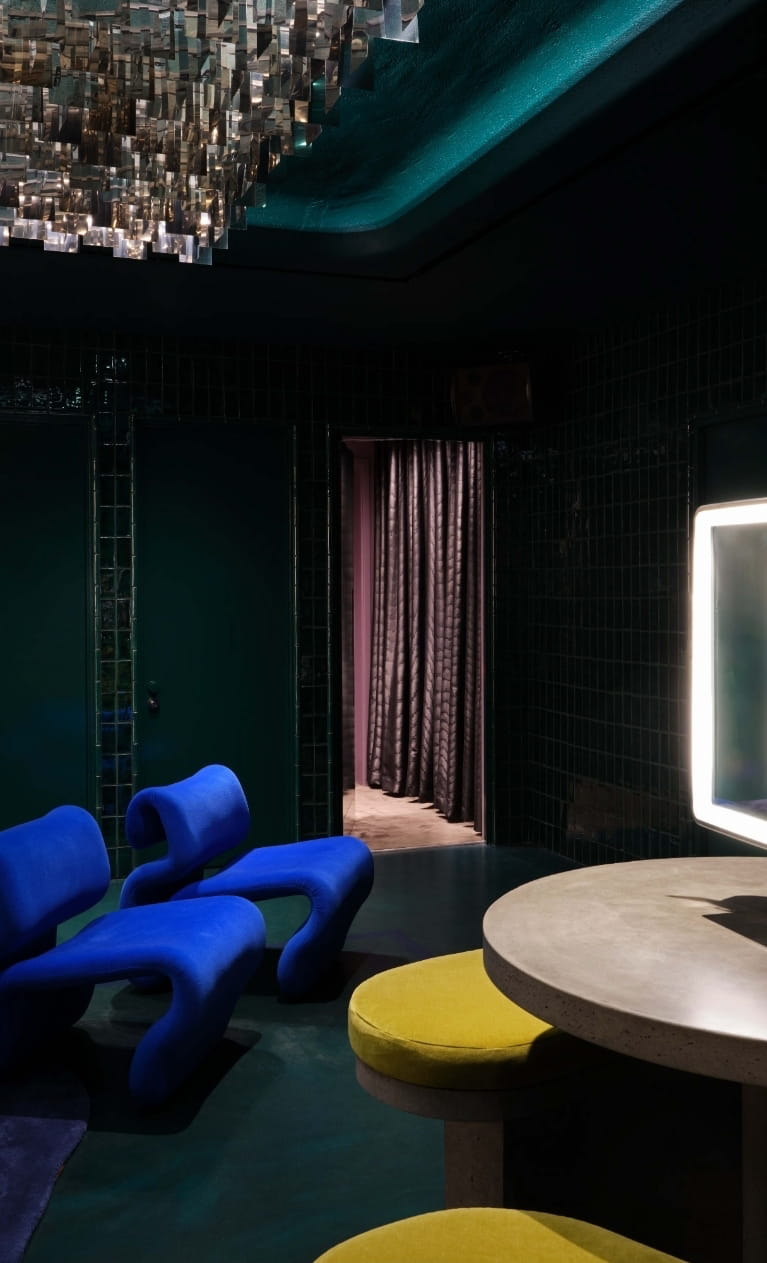 Emerald-tiled restroom lounge with cobalt chairs and a glowing vanity mirror at CoOc Members Club