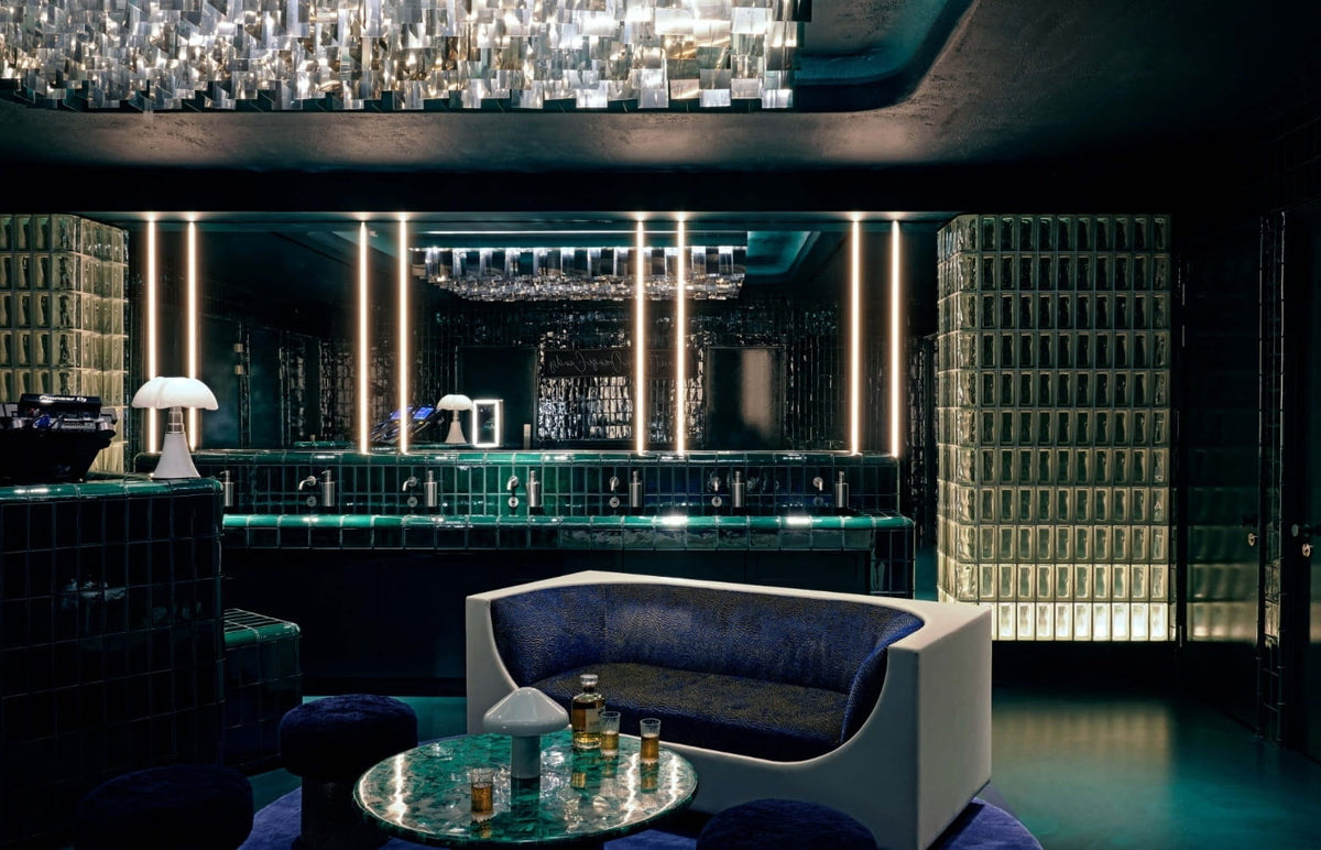 Green-tiled bathroom lounge with navy seating and a crystal chandelier at CoOc Members Club
