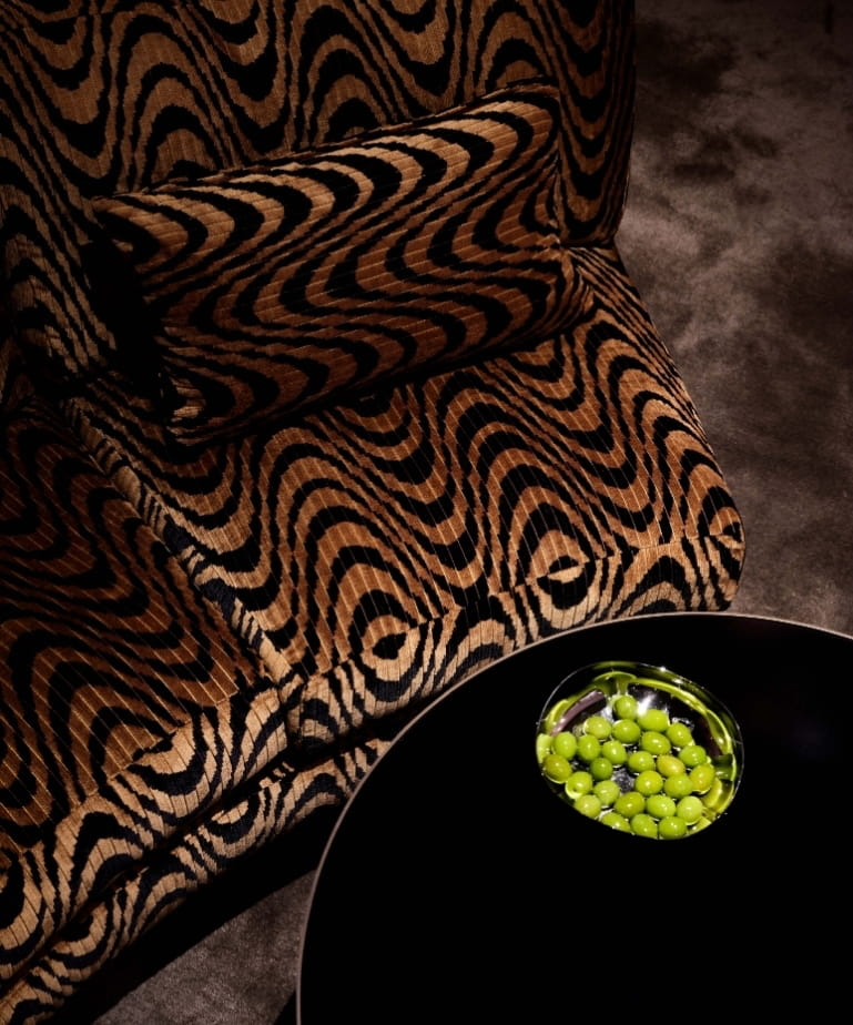 Close-up of a black-and-gold tiger-stripe armchair beside green grapes at CoOc Members Club