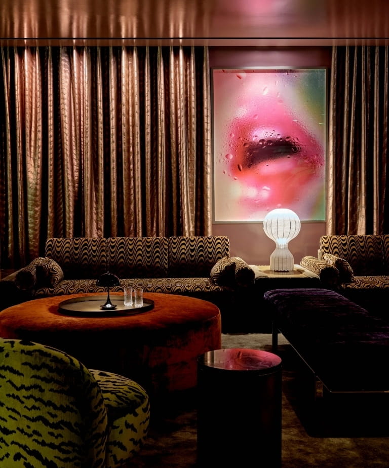 Lounge with tiger-stripe sofa, orange ottoman, and pink lips artwork at CoOc Members Club