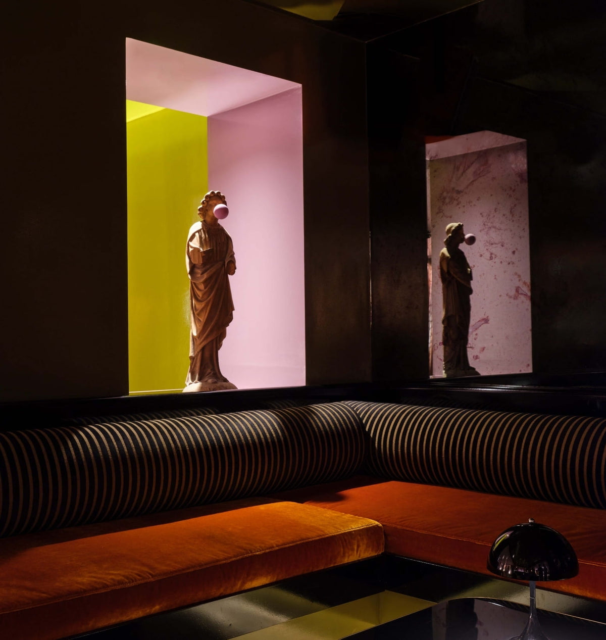 Orange velvet sofa facing a niche with a classical statue blowing bubblegum at CoOc Members Club