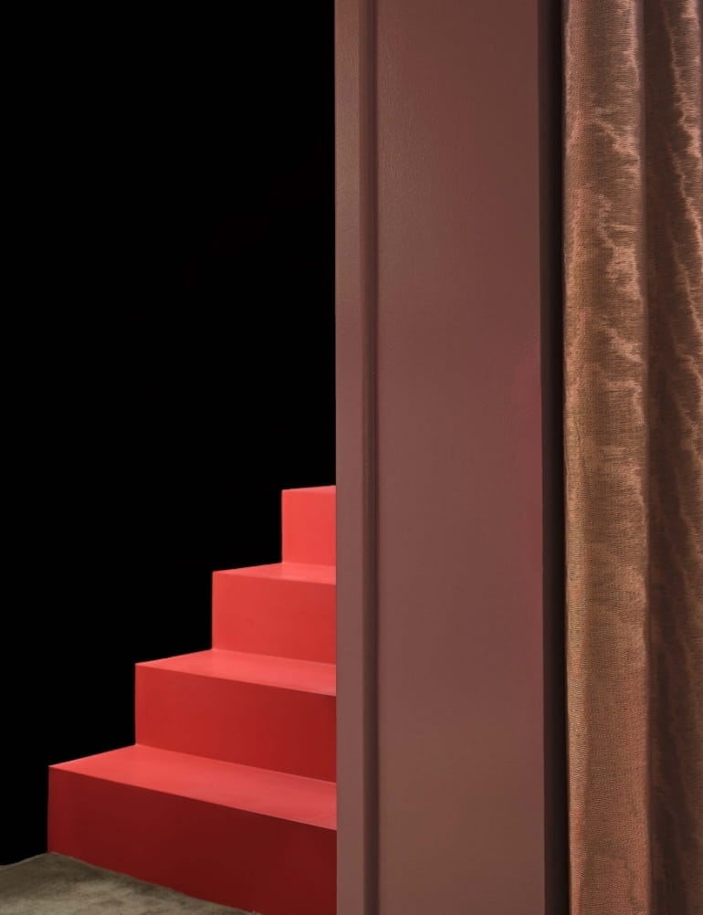Coral-red staircase against a black wall framed by bronze curtains at CoOc Members Club