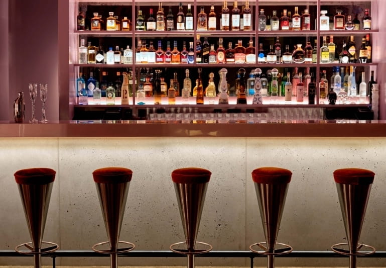 Bar with burgundy velvet stools and a backlit liquor wall at CoOc Members Club