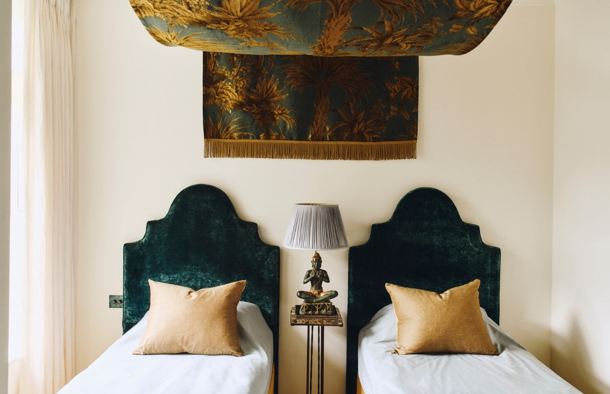 Twin beds with arched teal velvet headboards and a palm-print canopy in the Ladbroke Grove apartment