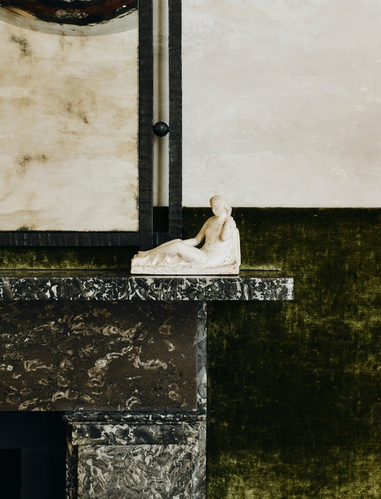 Marble mantel with a classical figurine against olive velvet walls in the Ladbroke Grove apartment