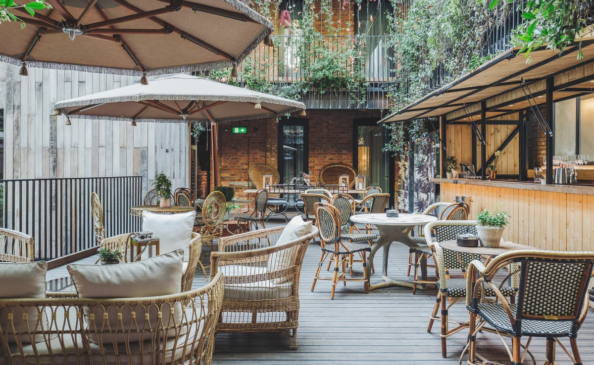 Courtyard terrace with rattan sofas, checkered bistro chairs, and trailing greenery at The Mandrake Hotel
