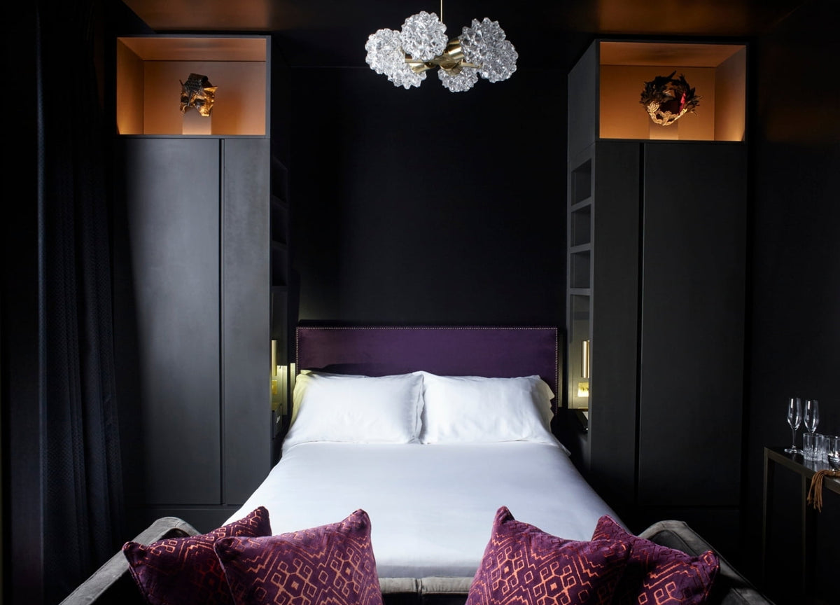 Dark bedroom with a purple velvet headboard and flanking cabinets at The Mandrake Hotel