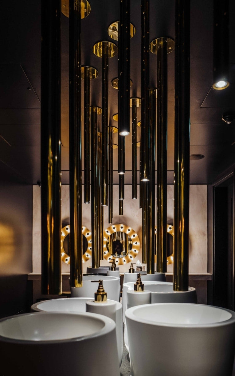 Restroom with suspended brass tubes and white pedestal basins at The Mandrake Hotel