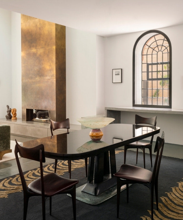 Glossy dining table facing a patinated brass fireplace and arched window in the North London warehouse