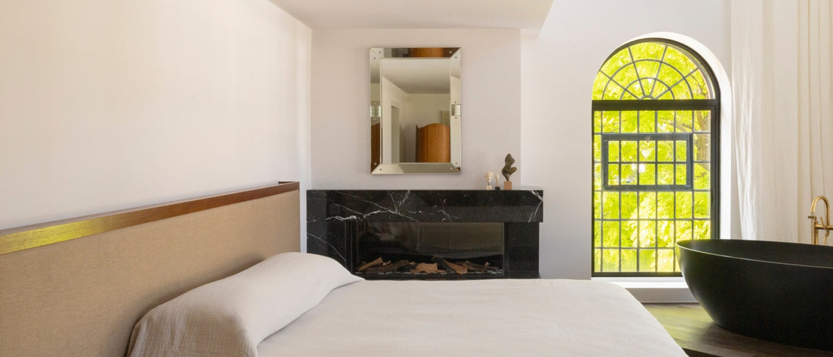 Bedroom with a black marble fireplace and matte black tub beside an arched window in the North London warehouse
