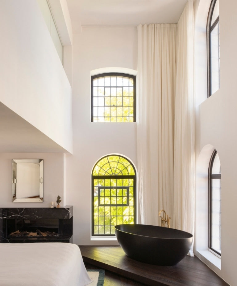 Matte black soaking tub on a dark wood platform in a double-height bedroom in the North London warehouse