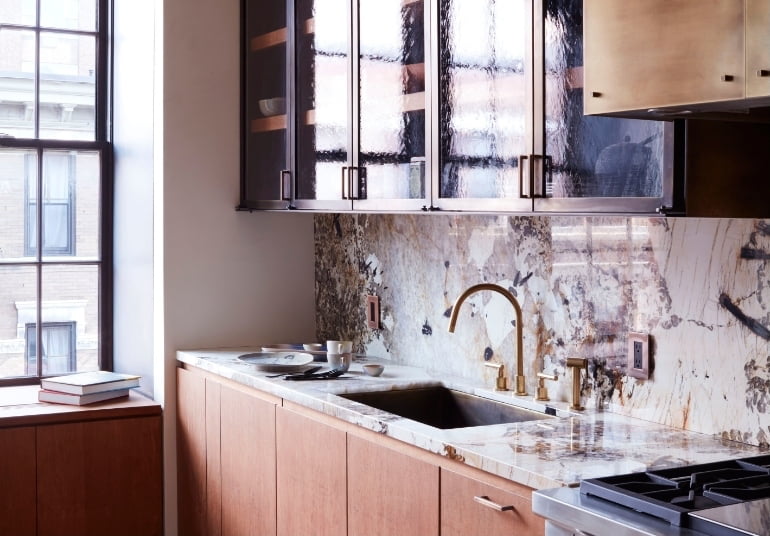 Kitchen with a veined stone backsplash, brass tap, and rippled-glass cabinets in the New York SoHo apartment