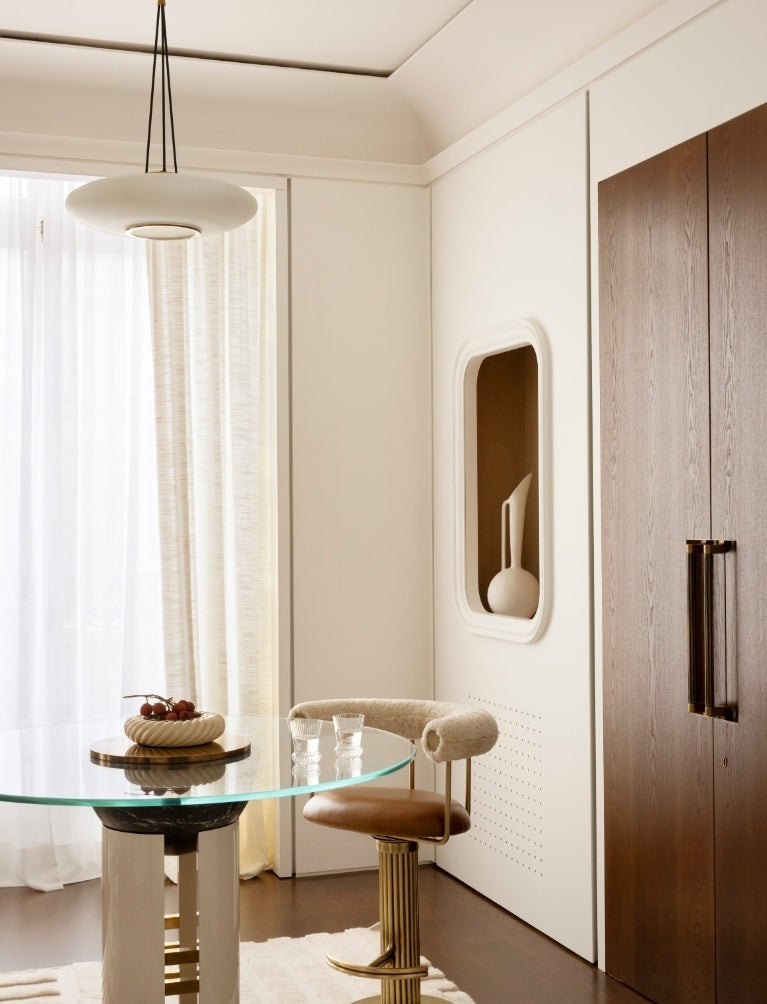 Breakfast nook with a round glass table and tan leather stool in the Paris 16th apartment