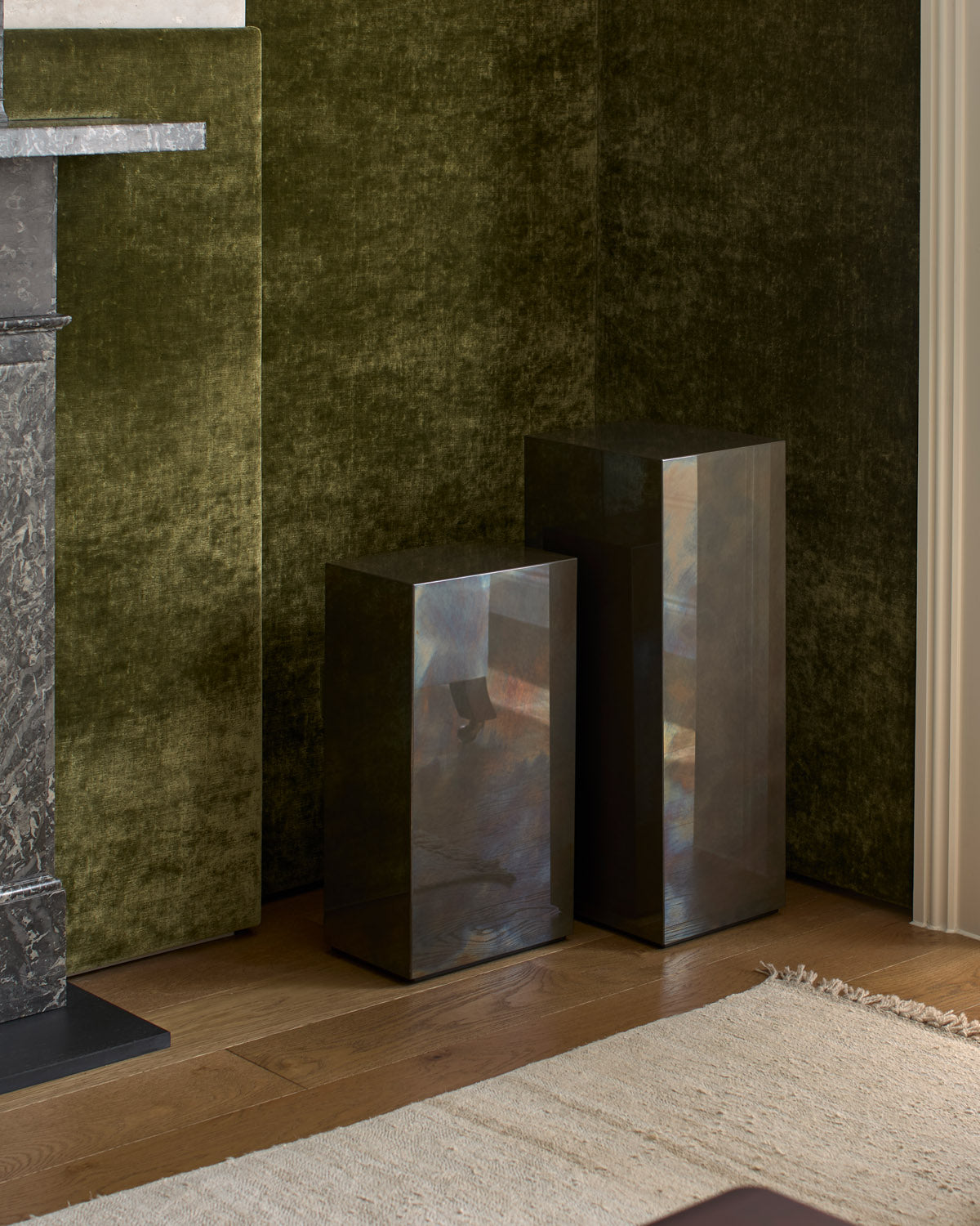 Tandem blocks in a green velvet alcove beside a marble fireplace, their surfaces reflecting the room