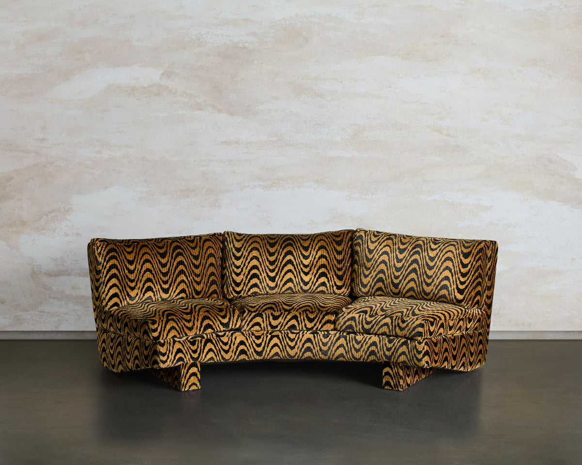 Front view of the Tripnotic sofa, a low curved three-seater in a gold and black pattern