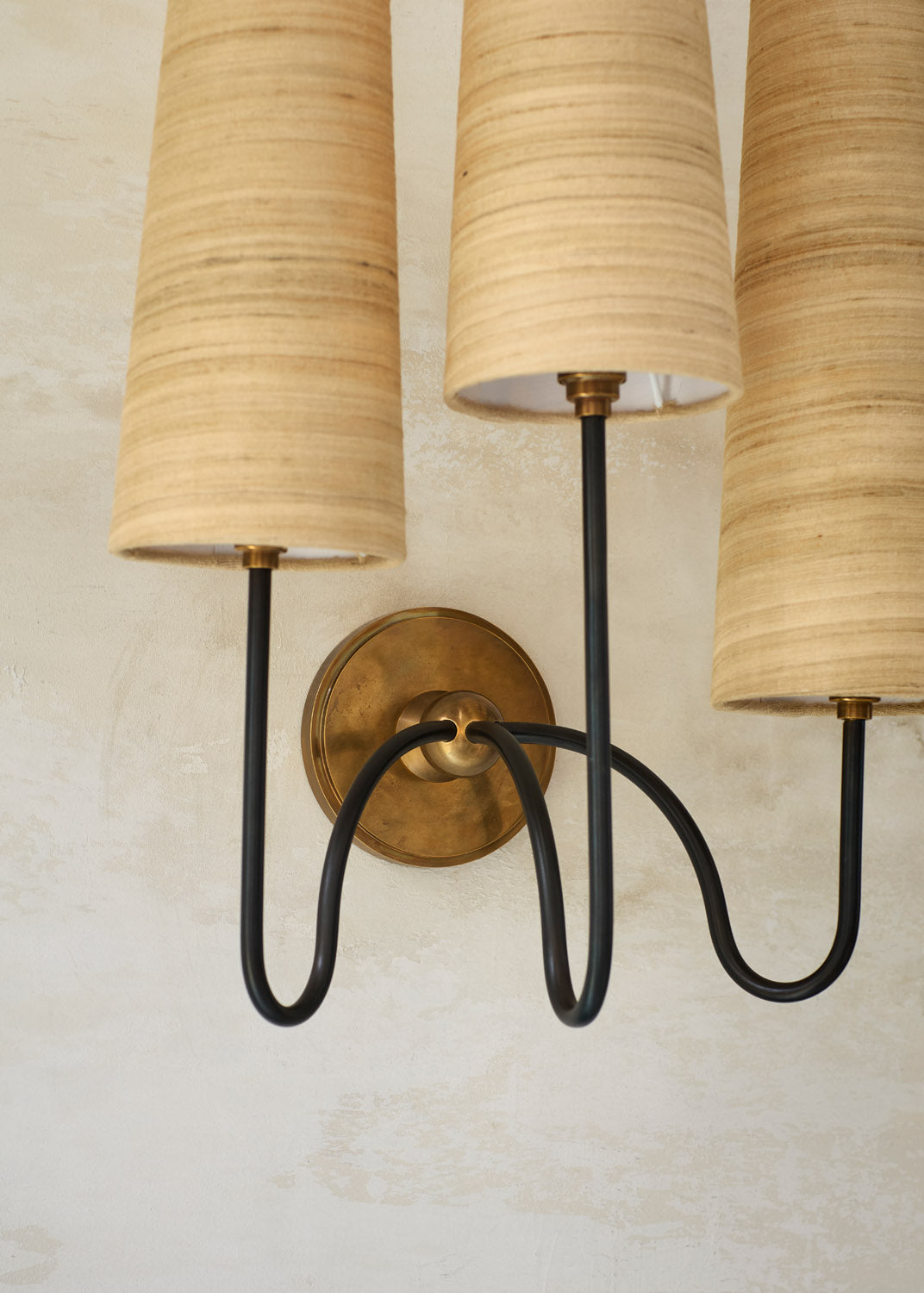 Detail of Union’s brass backplate and curved dark bronze arms beneath the silk shades