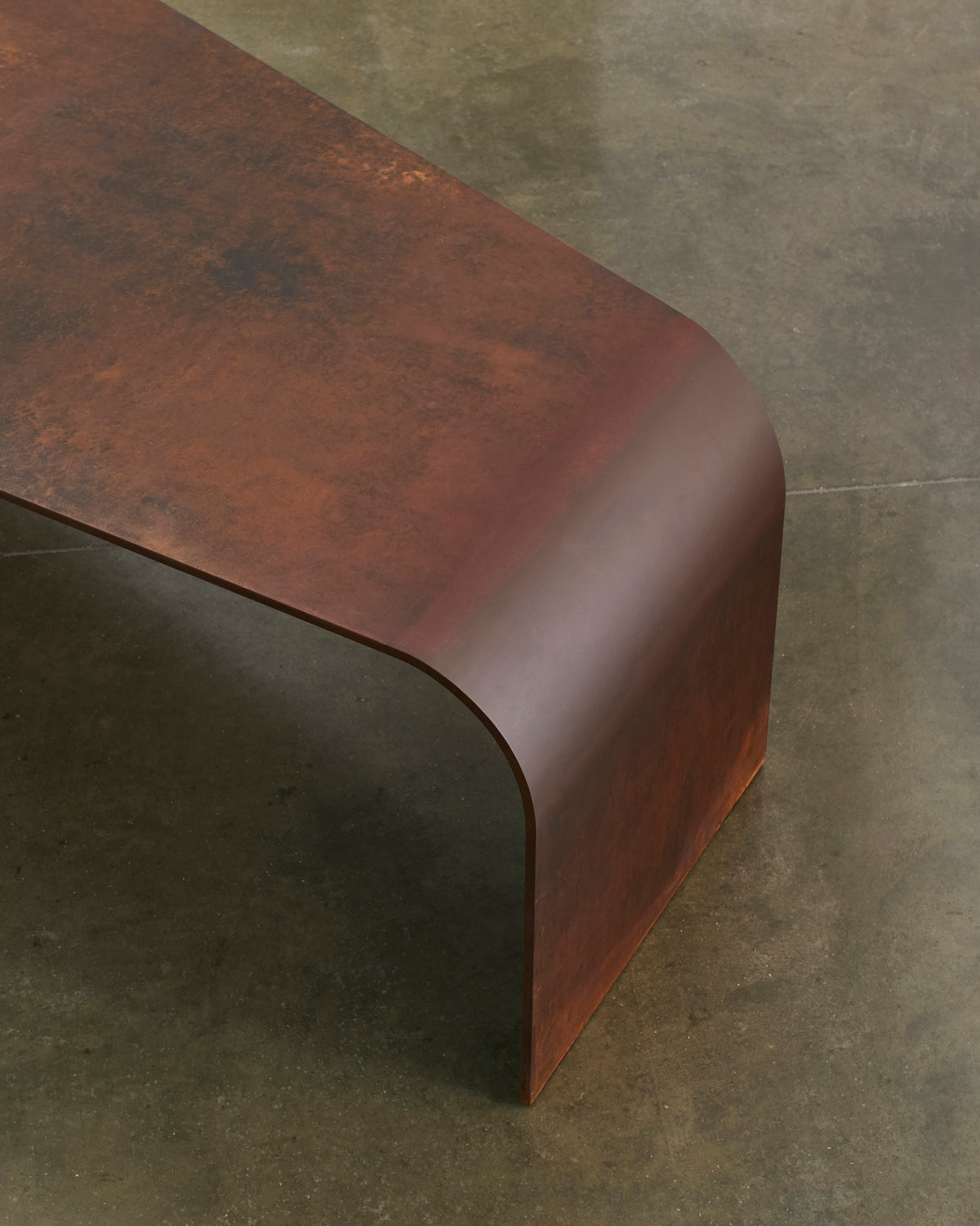 Close view of Perception’s rusted corten surface curving down to the concrete floor